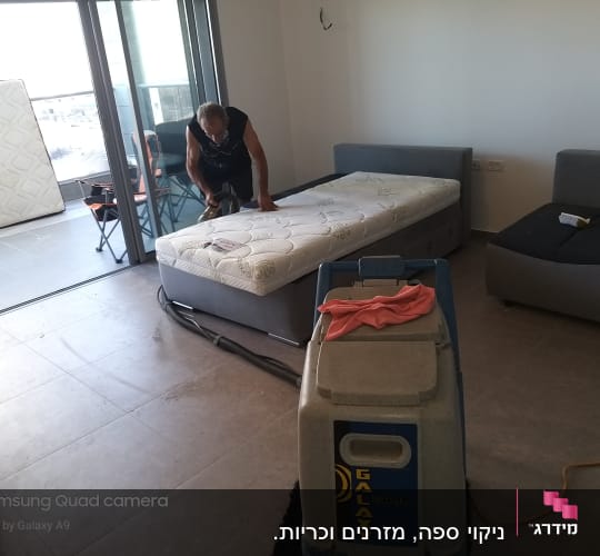 אדם מנקה מזרן עם שואב אבק מקצועי